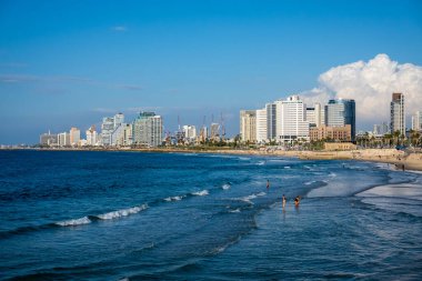 Tel Aviv, İsrail - 22 Kasım 2022: İsrail 'in Tel Aviv kentindeki bulutlu mavi gökyüzüne karşı kumlu sahilde deniz dalgaları üzerinde yürüyen turistlerin insansız hava aracı görüntüsü