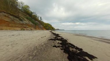 Fırtınalı bir kırsal günde bulutlu gökyüzüne karşı dalgalanan deniz kenarındaki lastik izleriyle tepenin ve kumlu plajın görüntüsü.
