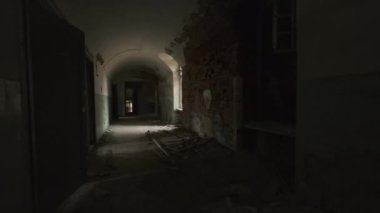 Handheld shot of walking inside of long empty passage with window and cracked walls in decay