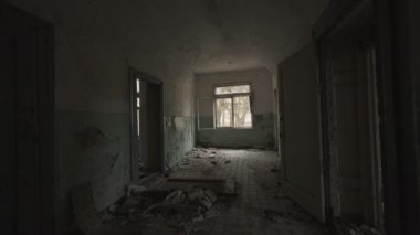 Uzun karanlık koridor, kırık duvarlı odalar ve yerdeki çöpler el kamerasıyla çekilmiş.