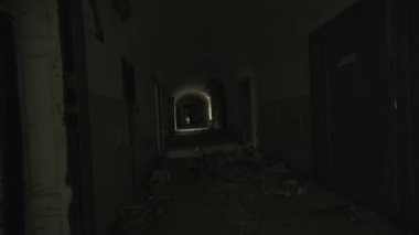 Pencere ve çatlak duvarlarla dolu uzun ve boş bir geçitte yürürken elde çekilmiş bir fotoğraf.