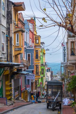 İstanbul, Türkiye - 15 Şubat 2023: Bulutlu gökyüzüne karşı tabelaları olan çok katlı çok katlı binalar arasındaki dar kasaba sokağı