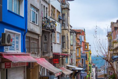 İstanbul, Türkiye - 15 Şubat 2023: Bulutlu bir günde küçük yerel dükkanların üzerinde tenteleri olan eski püskü binalar arasındaki dar sokak