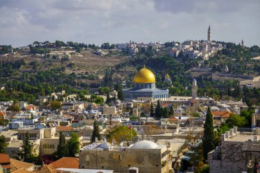 Eski Kudüs bölgesindeki tarihi tapınak ve kiliselerin manzarası. Bulutlu gökyüzünün altında binalar ve yeşil ağaçlar var.