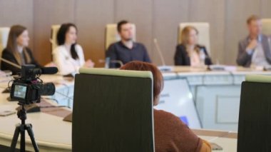 Toplantı sırasında video kamera tarafından kaydedilen konferans odasında, resmi giyinmiş, mikrofonlu meslektaşların sağ yumuşak odağı yuvarlak masada oturuyor.