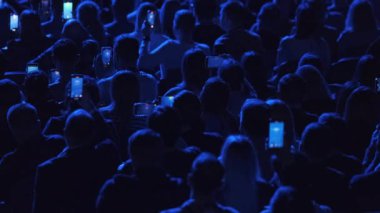 Yukarıdan gelen bir grup insan karanlık salonda şov izlerken video kaydetmek için cep telefonu kullanıyor.