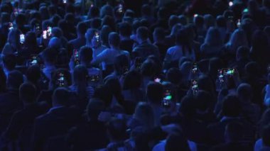 Yukarıdan gelen bir grup insan karanlık salonda şov izlerken video kaydetmek için cep telefonu kullanıyor.