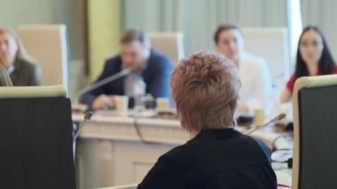 Konferans odasında mikrofonlarla iş stratejisinin detaylarını tartışırken, meslektaşların sağ yumuşak odağı yuvarlak masada toplanıyor.