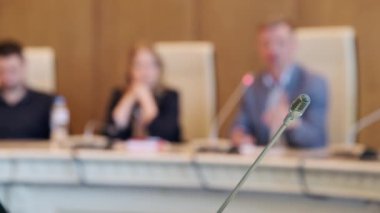 Seçici odak noktası sağda şık giyinen erkek ve bayan iş arkadaşlarının masada mikrofonlarıyla oturup iş görüşmesi sırasında iş raporları hakkında konuşmaları.