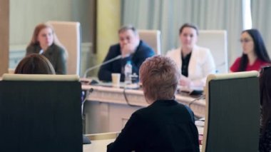 Konferans odasında mikrofonlarla iş stratejisinin detaylarını tartışırken, meslektaşların sağ yumuşak odağı yuvarlak masada toplanıyor.