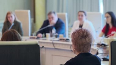 Konferans odasında mikrofonlarla iş stratejisinin detaylarını tartışırken, meslektaşların sağ yumuşak odağı yuvarlak masada toplanıyor.
