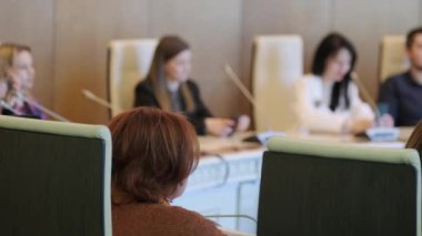 Konferans odasında mikrofonlarla iş stratejisinin detaylarını tartışırken, meslektaşların sağ yumuşak odağı yuvarlak masada toplanıyor.