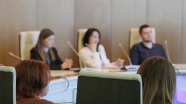 Konferans odasında mikrofonlarla iş stratejisinin detaylarını tartışırken, meslektaşların sağ yumuşak odağı yuvarlak masada toplanıyor.