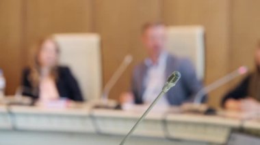 Seçici odak noktası sağda şık giyinen erkek ve bayan iş arkadaşlarının masada mikrofonlarıyla oturup iş görüşmesi sırasında iş raporları hakkında konuşmaları.