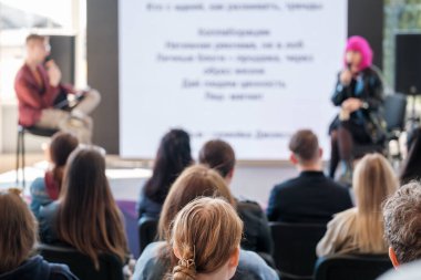 İsimsiz erkek ve kadın hoparlörler, geniş salondaki seminer sırasında sahnede monitörle oturup bir grup insana yeni iş stratejisi sunuyorlar.