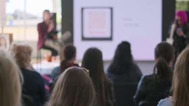 Tanımlanamayan kişilerin bulanık hoparlörleri dinlediği, ekranın yanında oturduğu ve toplantı sırasında konuşma yaptığı el kamerası görüntüsü.