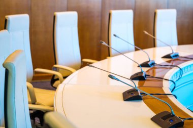 Yukardan yuvarlak şekilli masanın yanına yerleştirilmiş rahat deri koltuklardan geniş konferans odasına modern sınır mikrofonları yerleştirilmiş.