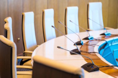 Yukardan yuvarlak şekilli masanın yanına yerleştirilmiş rahat deri koltuklardan geniş konferans odasına modern sınır mikrofonları yerleştirilmiş.