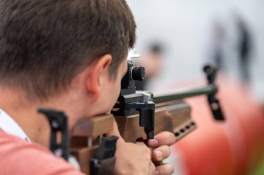 Siyah tişörtlü, tanınmayan erkek profesyonel nişancının arka plan görüşü açık havada bulanık arka planda hedefe şık bir silah doğrultuyor.