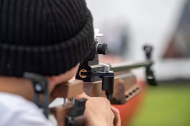 Siyah tişörtlü, tanınmayan erkek profesyonel nişancının arka plan görüşü açık havada bulanık arka planda hedefe şık bir silah doğrultuyor.