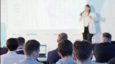 Sahnede durup seminer sırasında koridorda oturan insanlara iş projesini açıklayan kadın konuşmacının el kamerası görüntüsü.