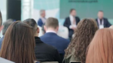 Sempozyum sırasında salonda oturup mikrofona konuşan insanların el kamerası görüntüsü.