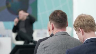 Seyirciler salonda otururken iş projesinden bahseden iş adamlarının el kamerasıyla çekilen hafif bir fotoğrafı.