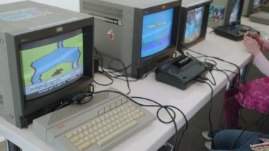 Moscow - June 6, 2023: Pan around real time of crop kids sitting at table playing videogames on old TVs using joysticks during festival