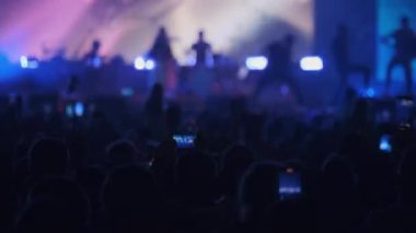 Arka planda, gece vakti sahnede parlayan neon ışıkları eşliğinde seyircilerin eğlenip dans ettiği görüntüler var.