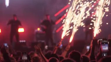 Gerçek zamanlı olarak bando sahnesinde müzik çalarken izleyiciler havai fişekler ve kollarla gece konserinde dans ederken.