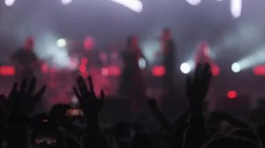 Grubun sahne arkası görüntüsü canlı konser sırasında seyirci ellerini kaldırıp dans ederken sahne ışıkları altında gerçek zamanlı.