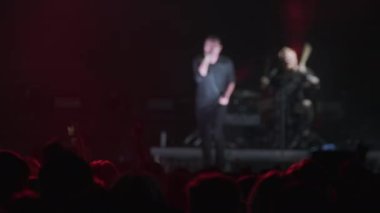 Davulcu ve şarkıcının konser sırasında neon ışığı eşliğinde sahnede enerjik bir şarkı söylerken, seyirci salonda dans ederken gerçek zamanlı el çekimi.