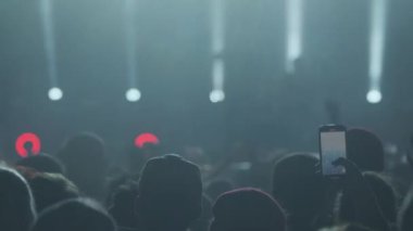 Sahnede bandonun sahne ışıkları altında dans ederken enerjik seyircilerin gerçek zamanlı kollarını kaldırması.