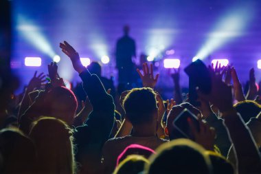 Heyecanlı anonim izleyicilerin el işaretlerini yükseltirken sahnede bulanık gitaristin aydınlık mavi ışıklarda seyirciyi akıllı telefonlarla alkışlaması.