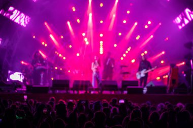 Sahne yakınındaki bir grup hayran ve gece parlayan kırmızı spot ışıklarıyla müzik grubu