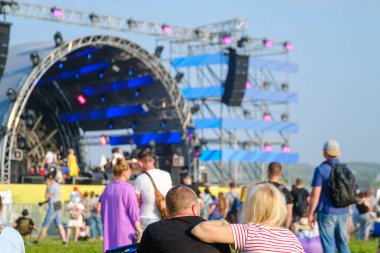 Güneşli yaz gününde mavi gökyüzüne karşı müzik festivali sırasında sahnenin yanında duran tanınmamış insanların arka görünüşü