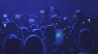 Modern müzik bandının performansını mavi neon ışıkta kaydetmek için cep telefonu kullanan insanların arka plan görüntüsü