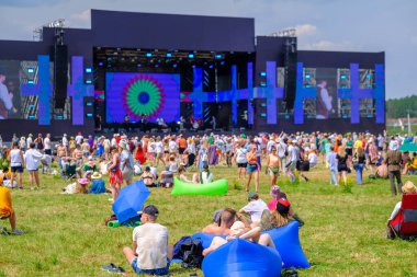 Müzik festivali sırasında dijital ekranlı muhteşem bir sahneyle yeşil alanda dinlenen ve gezinen bir kalabalık.