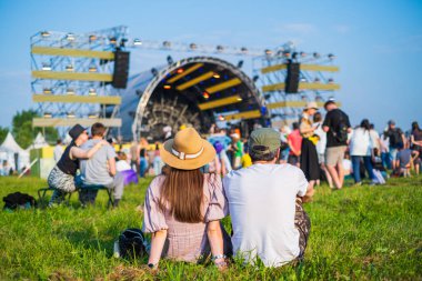 Güneşli bir yaz günü müzik festivali sırasında kalabalık ve sahnenin önünde sıradan giysiler içinde tanınmayan bir çiftin arka planda oturuşu.