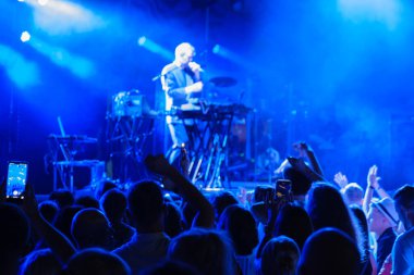 Klüpteki erkek şarkıcı ve müzisyen konserinde sahne kenarında dururken, tanınmayan insanların kollarını kaldırarak dans edişlerinin arka planı.