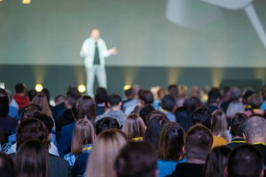 Küresel bir konferans salonunda sunum sırasında sahnede erkek konuşmacıları dinleyen iş insanlarının geçmişe bakış 
