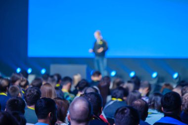 Küresel bir konferans salonunda sunum sırasında sahnede erkek konuşmacıları dinleyen iş insanlarının geçmişe bakış 