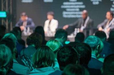 İş konferansına katılan profesyonellerden oluşan bir kalabalık panel tartışmasındaki konuşmacılara odaklanıyor. İlgili izleyiciler, sektör liderlerini dikkatle dinliyor..