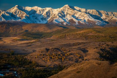 Sonbaharda karla kaplı tepeleri olan görkemli Altai dağlarının büyüleyici manzarası. Canlı renkleri ve yuvarlanan tepeleri olan manzara güzelliği.