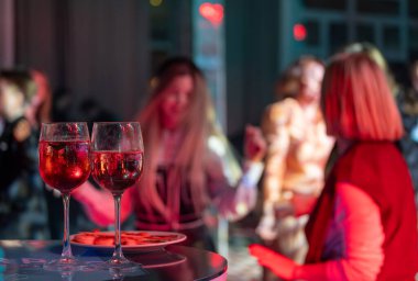 İki kadeh kırmızı şarap ve bulanık bir parti sahnesinin önünde insanlarla bir tabak.