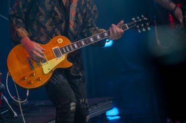 Müzisyen canlı performans sırasında tutkuyla elektro gitar çalıyor. Konserde enstrüman ve müzisyenlere odaklanan canlı bir atmosfer.