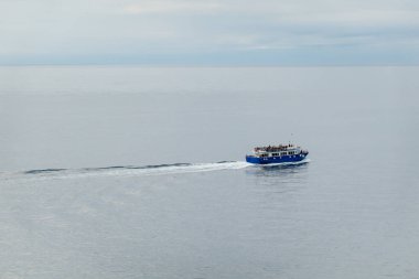 Blue ferry sails peacefully across calm open sea with scattered passengers onboard enjoying a serene journey. clipart