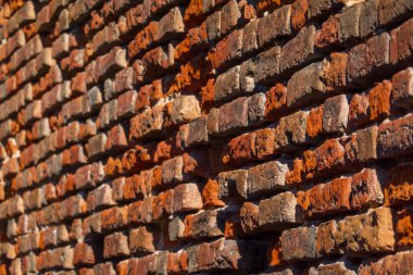 Engebeli kırmızı tuğla duvarın detaylı görüntüsü eşsiz bir doku ve sıcak tonlama gösteriyor. Doğal ışık karmaşık yüzeyi vurgular, mimari tasarımda derinlik ve karakter izlenimi yaratır..