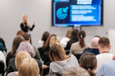 Bir konferans ortamında iş sunumunu dinleyen insanların bulanık görüntüsü. Konuşmacı öğrenmeye ve ilgilenmeye istekli izleyicilere bilgilendirici slaytlar sunuyor..