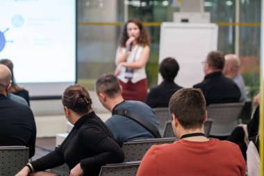 Diverse group participating in a business seminar, focusing on speaker presentation. Audience engaged, learning in a professional setting with visual aids enhancing understanding and collaboration. clipart